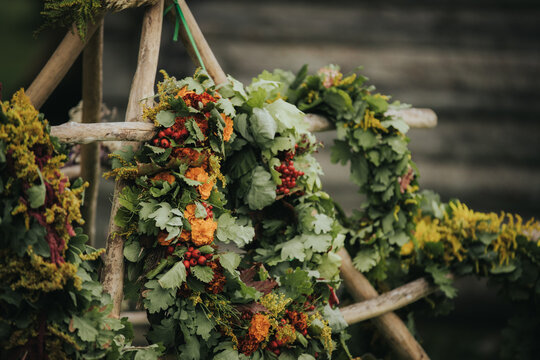 Decorative floral wreath made of green leaves, orange flowers, and red berries hanging on a wooden frame in a natural outdoor setting