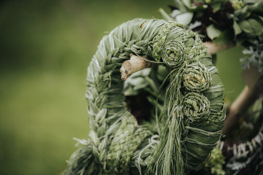 Decorative green wreath made of woven grass and leaves, featuring intricate spiral patterns, displayed against a blurred natural background