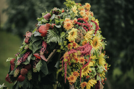 Colorful floral arrangement featuring sunflowers, ferns, and various blooms displayed outdoors in a lush green setting, showcasing vibrant colors and natural textures