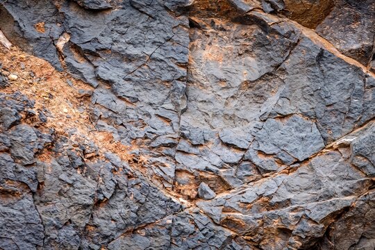 Full frame close up of cracked dark rock surface with orange soil and textured fractures