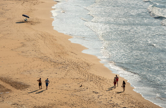 Group of unrecognised people strolling on the sand beside the sea on a sunny day