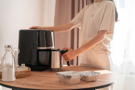 A person operates an air fryer on a wooden table while preparing meals in a home kitchen setting