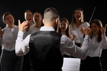 Obraz premium Leadership and teamwork, music conductor leading a choir with passion and precision during a performance on a dark stage with professional lighting