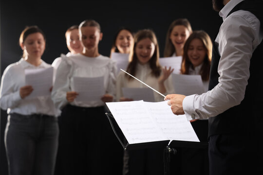 Choir performance and musical leadership, conductor directing a singing group with sheet music in a concert hall setting