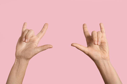 Rock and roll lifestyle and music culture, two hands showing heavy metal sign with fingers raised on a solid pastel pink background