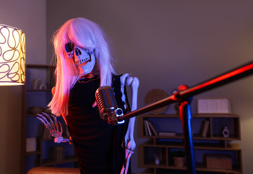 Human skeleton model dressed as woman with microphone in dark living room