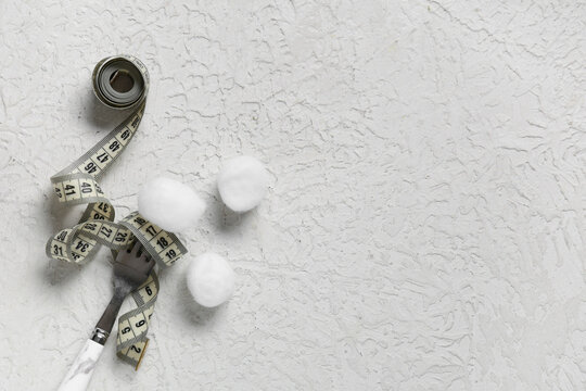 Cotton balls with fork and measuring tape on grunge white background. Unhealthy diet concept