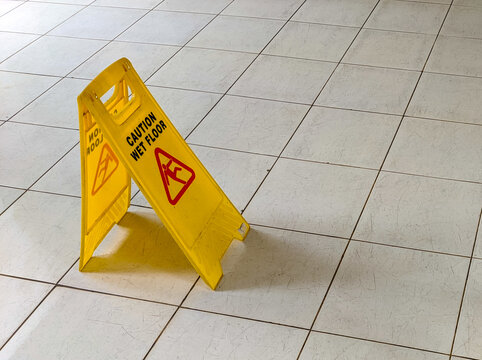 Yellow caution sign warning of wet floor placed on tiled surface, highlighting safety awareness to prevent slips and falls in indoor public spaces with clear visual instruction.