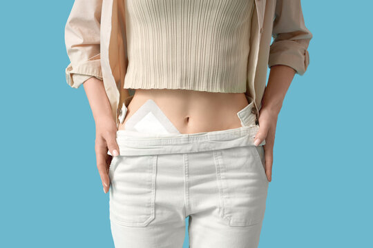 Young woman with applied medical patch after appendectomy surgery on blue background, closeup