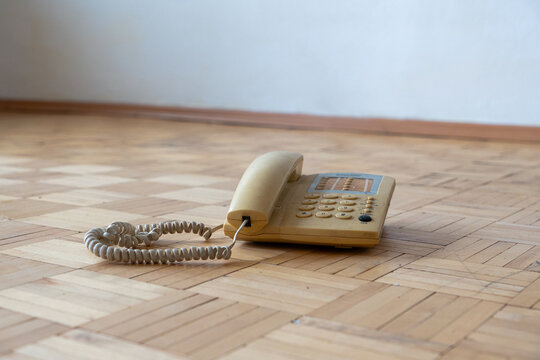 Old apartment interior with outdated landline telephone on worn parquet floor, neglected residential space requiring renovation and home refurbishment