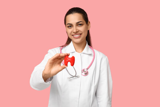Portrait of female doctor with thyroid model on pink background