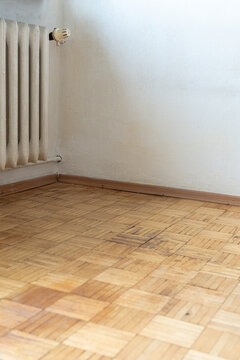 Old apartment interior with worn herringbone parquet floor and outdated radiator, empty room with aged walls requiring renovation and remodeling
