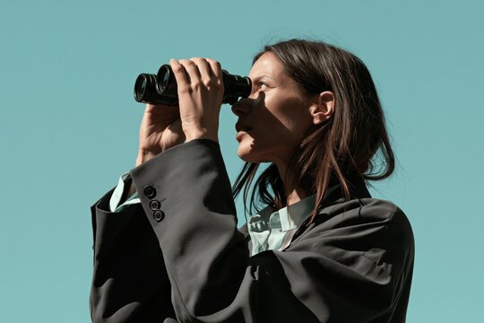 Businesswoman looking through binoculars against a clear teal sky for background and banner design
