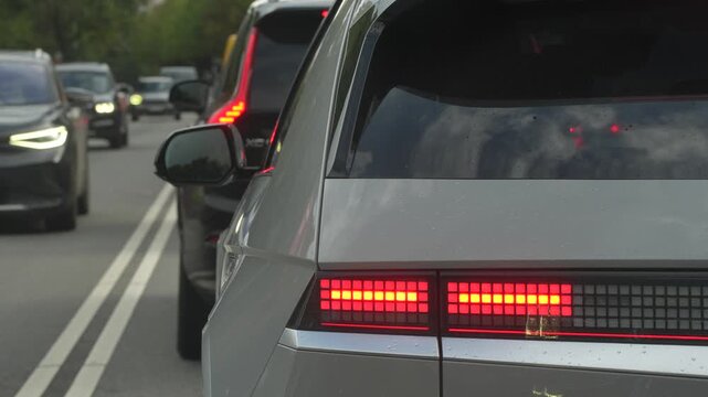 Rear lamp array on a queued hatchback remains illuminated while oncoming cars advance, showing vehicle signaling and contrasting traffic flow along a shared road