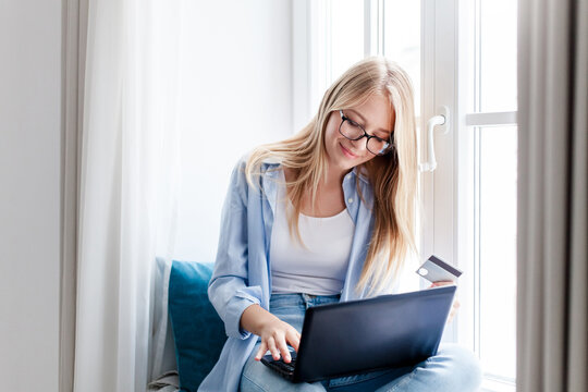 Woman using laptop and credit card for purchases. Shopping online at home. Happy girl investing. Technology lifestyle for finance, e-commerce, banking