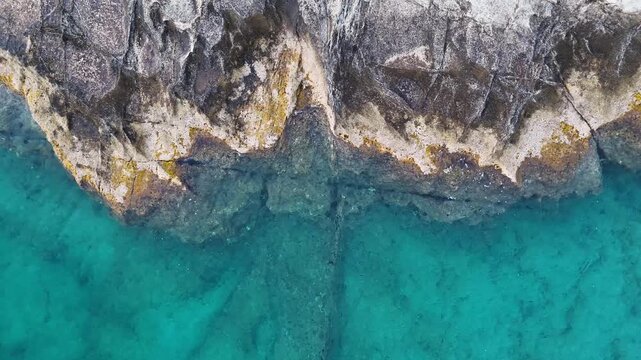Aerial drone view looking down on the unique rocky landscape and the azure Aegean sea surrounding the Greek island of Milos in Greece. The ocean is clear blue. 
