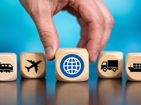 Hand placing a wooden globe block above transportation symbols, representing global logistics and international trade.