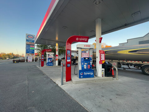 gananoque, canada - October 22 2022: Esso gas station, at sunset. Multiple fuel pumps stand under a canopy. A large fuel tanker truck is parked by the pumps.
