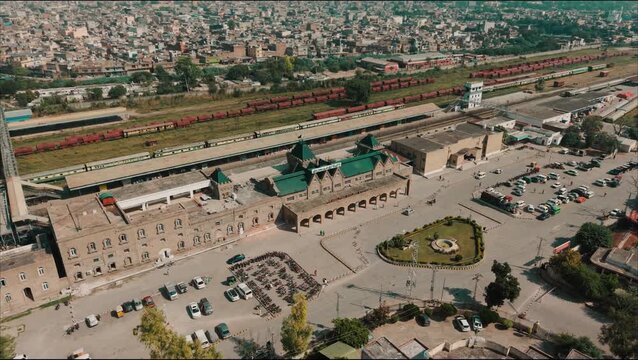 Aerial view of Rawalpindi Railway Station building, surrounding urban landscape, and long freight train carriages on parallel railway lines.