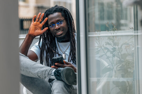 young african man sitting on a terrace with a mobile phone waving