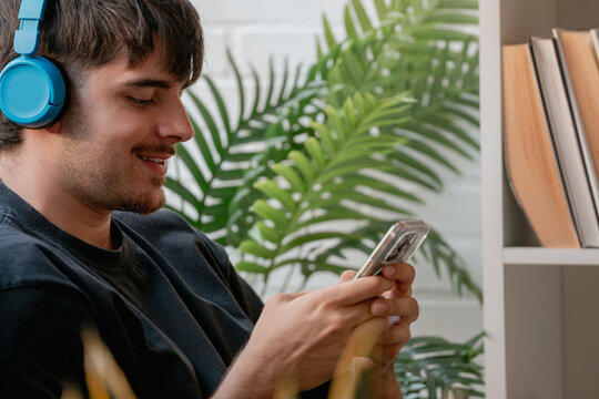 Young man wearing headphones and using a smartphone while relaxing at home