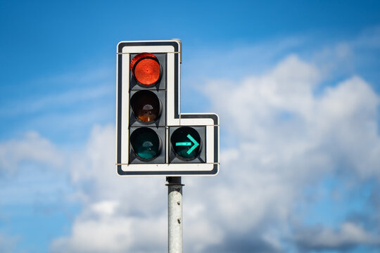 Traffic signal displaying a red stop light and an illuminated right turn arrow, illustrating separate directional control and vehicle movement at a road junction