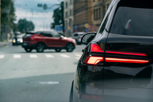 Passenger vehicle with illuminated rear lamps waiting at an urban intersection as another car crosses, illustrating junction traffic flow and vehicle signaling