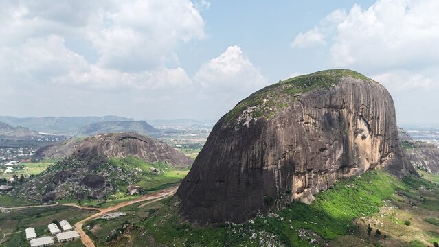 Aerial view of a massive granite rock formation surrounded by green farmland and a sprawling Nigerian landscape.