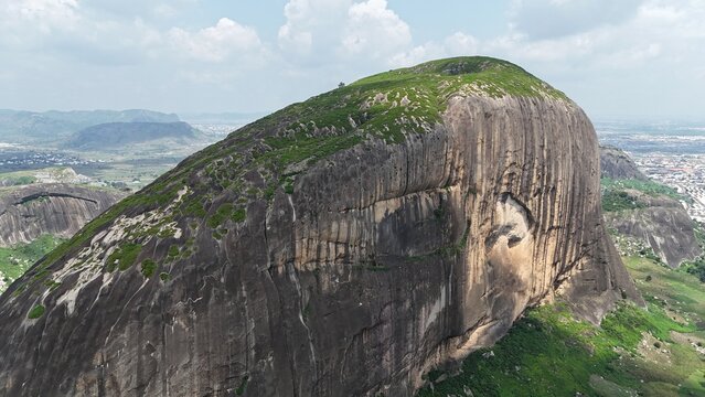 Aerial view of a massive granite rock formation surrounded by green farmland and a sprawling Nigerian landscape.