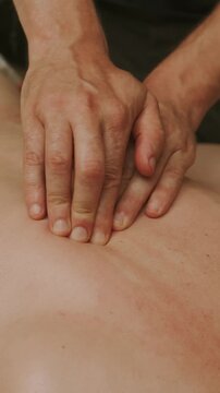 close-up of adult hands press palms firmly on bare upper back in indoor massage therapy to relieve stress