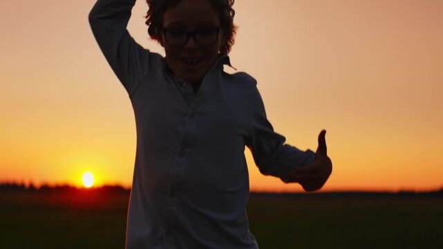 Joyful child running through open field at vibrant sunset, playful silhouette against glowing orange sky capturing carefree childhood freedom and outdoor adventure