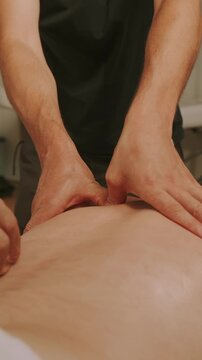 closeup of therapist palms and thumbs applying steady pressure to client's lower back in calm treatment rooms