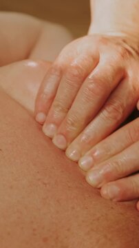 close-up view of two hands applying firm pressure and gliding strokes across tanned back under warm spa light