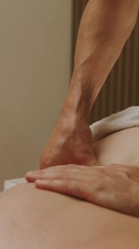 close-up of massage therapist hands pressing into lower back and hip of person lying face down under warm