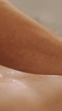close-up hands press and smooth massage oil across bare skin on horizontal surface in soft warm light