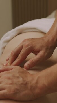 hands pressing gently on lower abdomen near navel as person lies face up on treatment table warm light