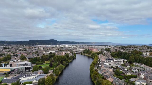Elevated wide aerial drone video of River Ness flowing through Inverness cityscape, Kessock Bridge, Beauly Firth, and Highland hills in Scotland