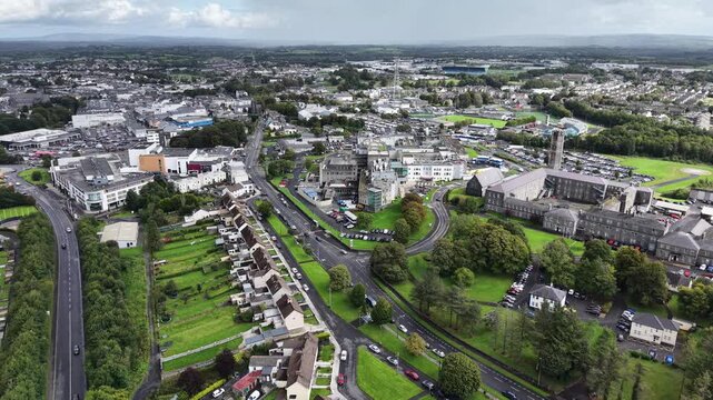 Aerial drone footage overlooking Castlebar town centre in County Mayo, Ireland, showcasing historic stone buildings, residential neighborhoods, busy roads, green parks, and the surrounding Irish