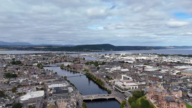 Elevated wide aerial drone shot of Inverness cityscape, River Ness, Kessock Bridge, and Moray Firth under cloudy sky in Highland, Scotland