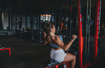 Three quarter back view of Hispanic woman doing lat pulldown exercise on machine, athletic female...