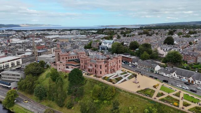 High wide aerial drone parallax orbit footage of Inverness Castle overlooking Moray Firth, River Ness, and city landscape in Highland, Scotland