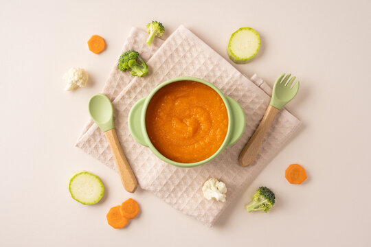 Baby's first feeding: homemade carrot puree in green bowl with spoon and spork for weaning