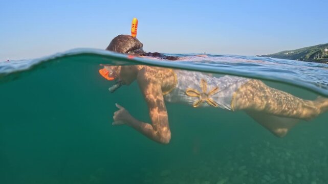 A happy girl in a mask with a snorkel is swimming underwater. Half underwater scene of little girl with diving mask and snorkel swimming in turquoise tropical sea water of exotic island. Slow motion