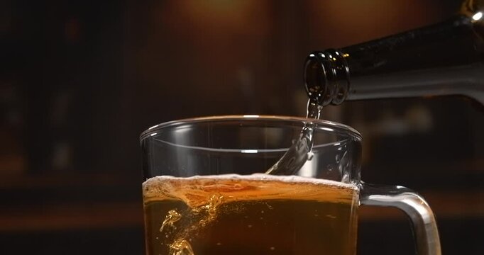 Beer pouring from glass bottle into mug in slow motion