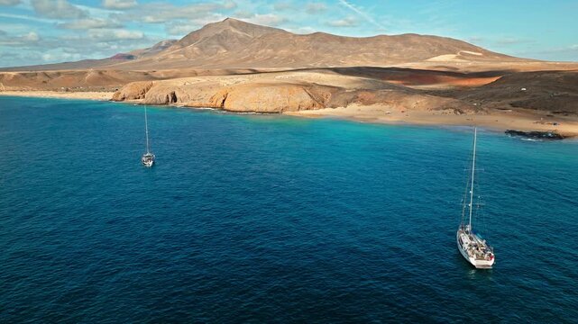Drone view of boats off Playa de Papagayo in Lanzarote. Deep blue water, sandy coves and barren volcanic hills create a beautiful coastal holiday landscape.