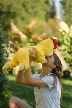 Happy mother holding cute baby in yellow chicken costume outdoors in park on sunny day