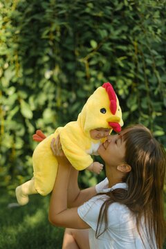 Happy mother holding cute baby in yellow chicken costume outdoors in park on sunny day
