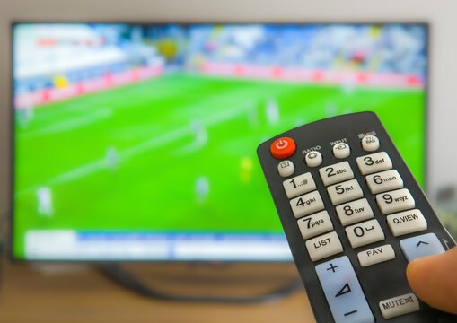 Close Up of Hand Holding Remote Control with Blurred Television Screen in Background