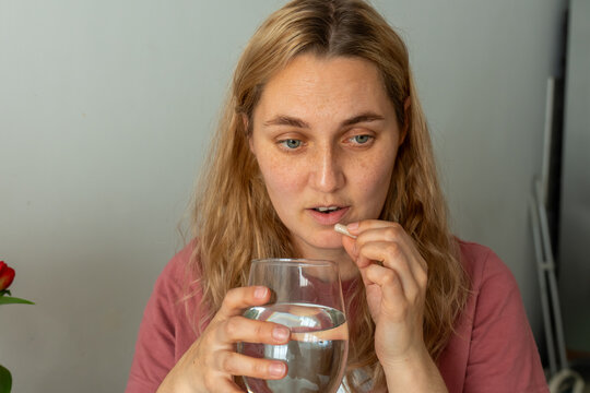 Woman taking a dietary supplement capsule with a glass of water at home. Concept of daily vitamin intake, healthy habits, nutritional support, personal healthcare and wellness routine.