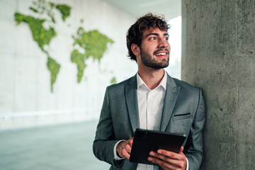 Young businessman holding tablet, smiling, looking away, planning global business strategy